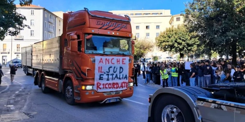 Truck participating in a transport strike demonstration in southern Italy, with protesters gathered alongside the road.